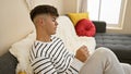 Handsome, young hispanic man, engrossed in serious expression, sitting on living room sofa, indoors; a worried portrait depicting Royalty Free Stock Photo