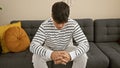 Handsome, young hispanic man, engrossed in serious expression, sitting on living room sofa, indoors; a worried portrait depicting Royalty Free Stock Photo