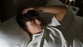 Handsome, young hispanic teenager lying comfortably in bed, engrossed in deep thought under a cozy blanket in a well-lit bedroom, Royalty Free Stock Photo