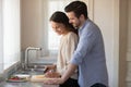 Loving affectionate millennial newlyweds preparing meal together at home.