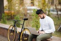 Handsome young indian businessman dressed in suit working on laptop computer while sitting outdoors near bicycle Royalty Free Stock Photo