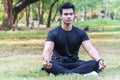 Young indian guy practicing yoga in the park Serene yoga man practitioner workout and sitting in lotus pose or asana with Royalty Free Stock Photo