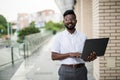 Handsome young indian hipster man holding his laptop while standing on the street near bussines office Royalty Free Stock Photo