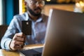 Handsome young indian man with credit card and phone in hands doing purchases during online shopping Royalty Free Stock Photo