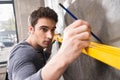 Handsome young laborer with pencil measuring wall with level tool Royalty Free Stock Photo