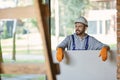 Handsome young male builder in hard hat looking positive, holding drywall while working at construction site