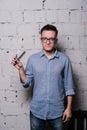 Handsome young male hairdresser in glasses, posing with scissors and comb, on gray brick wall background, vertical image Royalty Free Stock Photo