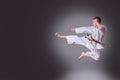 Handsome young male karate player doing kick on the gray background