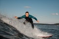 Handsome young male surfer stands in the spray of a wave, riding it on a surfboard Royalty Free Stock Photo