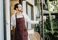 Handsome young man in apron working waitress in cafe opening entrance door and inviting customers to his shop. Cheerful owner of Royalty Free Stock Photo