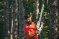 Handsome young man with axe near forest. Logging. Deforestation. Professional lumberjack holding chainsaw in the forest