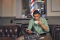 Handsome young man in a barbershop is waiting for the master in the waiting room while drinking coffee