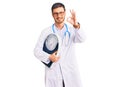 Handsome young man with bear as nutritionist doctor holding weighing machine doing ok sign with fingers, smiling friendly