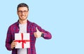 Handsome young man with bear holding gift smiling happy and positive, thumb up doing excellent and approval sign Royalty Free Stock Photo