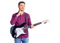 Handsome young man with bear playing electric guitar serious face thinking about question with hand on chin, thoughtful about Royalty Free Stock Photo