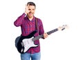 Handsome young man with bear playing electric guitar smiling happy doing ok sign with hand on eye looking through fingers Royalty Free Stock Photo