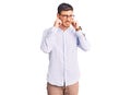 Handsome young man with bear wearing elegant business shirt and glasses covering ears with fingers with annoyed expression for the Royalty Free Stock Photo