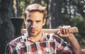 A handsome young man with a beard carries a tree. Handsome Woodworkers lumberjack plaid shirt holding the axe on green Royalty Free Stock Photo