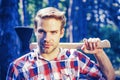 A handsome young man with a beard carries a tree. Handsome Woodworkers lumberjack plaid shirt holding the axe on green Royalty Free Stock Photo