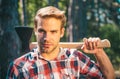 A handsome young man with a beard carries a tree. Handsome Woodworkers lumberjack plaid shirt holding the axe on green Royalty Free Stock Photo