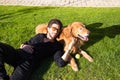 Handsome young man with beard and glasses lying on the grass sunbathing with his brown golden retriever dog. Concept pets, animals Royalty Free Stock Photo