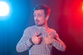 Handsome young man with beard hipster in a plaid shirt posing on a blue-red background and showing thumbs up. Concept of Royalty Free Stock Photo