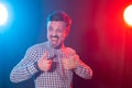 Handsome young man with beard hipster in a plaid shirt posing on a blue-red background and showing thumbs up. Concept of Royalty Free Stock Photo