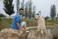 Handsome young man with beard and his large dog sitting on rocks looking back. The dog is a brown Labrador retrieve. Concept pets