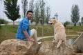 Handsome young man with beard and his large dog sitting on rocks looking back. The dog is a brown Labrador retrieve. Concept pets