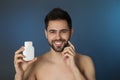 Handsome young man with beard holding post shave lotion on blue background