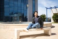 Handsome young man with beard, sunglasses, leather jacket and jeans, sitting on a stone bench, relaxed. Concept beauty, fashion, Royalty Free Stock Photo