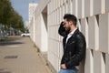 Handsome young man with beard, sunglasses, leather jacket, white shirt and jeans, leaning against a wall of white stone blocks, Royalty Free Stock Photo