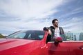 Handsome young man with beard, sunglasses, leather jacket and white shirt, leaning on the roof of his red sports car. Concept