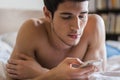 Handsome young man in bed typing on cell phone Royalty Free Stock Photo