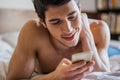 Handsome young man in bed typing on cell phone Royalty Free Stock Photo