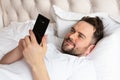 Handsome young man in bed typing on cell phone Royalty Free Stock Photo