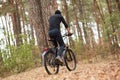 Handsome young man biking in countryside, guy wearing black sportwear and cap posing backwards around trees in wood, spending