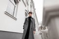 Handsome young man in black clothes in an elegant gray plaid coat with a trendy hairstyle walks on the street near a vintage white Royalty Free Stock Photo