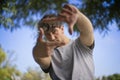 A handsome young man blinks his eyes and looks through a frame made up of hands