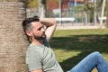 Handsome young man with blue eyes, beard, green T-shirt and jeans, sitting and leaning on a palm tree trunk, sleeping. Concept Royalty Free Stock Photo