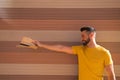 A handsome young man with blue eyes and a beard and a yellow T-shirt stretches out his arm with a hat in his hand. In the Royalty Free Stock Photo