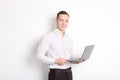 Smiling confident young man, no tie, holding grey laptop device and typing while standing against solid white wall. Wireless inter Royalty Free Stock Photo