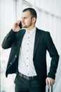 Handsome young man on business trip walking with his luggage and talking on cellphone at airport. Travelling businessman making ph Royalty Free Stock Photo