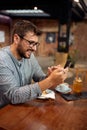 Handsome young man at cafe, sitting alone at table scrolling on his phone. Coffee break Royalty Free Stock Photo