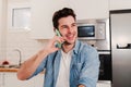 handsome young man calling by cellphone and smiling at home kitchen. Caucasian male using a mobile phone to have a Royalty Free Stock Photo