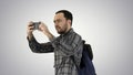 Handsome young man carrying backpack and taking a picture of himself on gradient background. Royalty Free Stock Photo