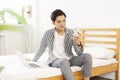 Handsome young man in casual clothes sitting on the bed,with a laptop in bedroom, play mobile games and chat on the phone Royalty Free Stock Photo