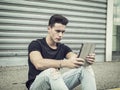 Young man using tablet PC sitting on street curb Royalty Free Stock Photo