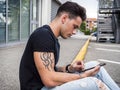 Young man using tablet PC sitting on street curb Royalty Free Stock Photo