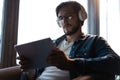 Handsome young man in casual clothes using a digital tablet and headphones and smiling while sitting on the chair. Royalty Free Stock Photo